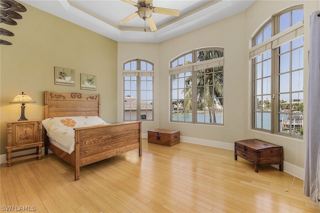 bedroom with ceiling fan, a raised ceiling, and light hardwood / wood-style floors