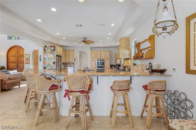 kitchen with a raised ceiling, custom exhaust hood, backsplash, and a breakfast bar