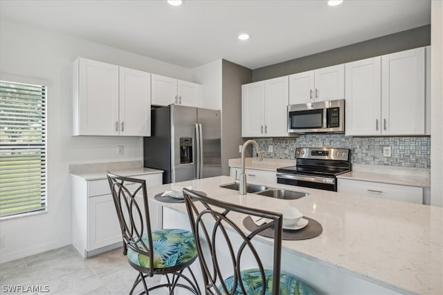 kitchen with white cabinetry, appliances with stainless steel finishes, sink, light tile flooring, and a kitchen bar