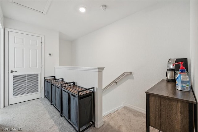 hallway featuring attic access, an upstairs landing, baseboards, and light colored carpet