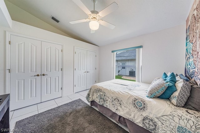 tiled bedroom featuring vaulted ceiling, ceiling fan, and multiple closets