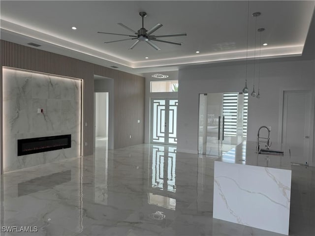 unfurnished living room featuring sink, a high end fireplace, a raised ceiling, and ceiling fan