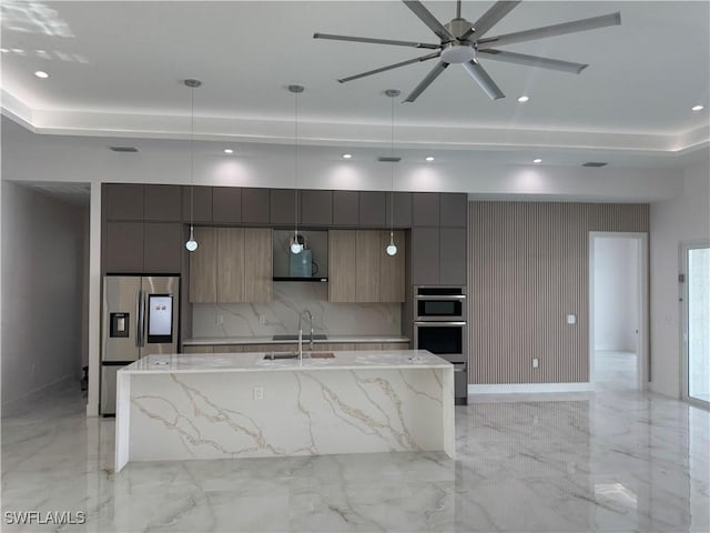 kitchen with stainless steel appliances, decorative light fixtures, light stone countertops, and a kitchen island with sink