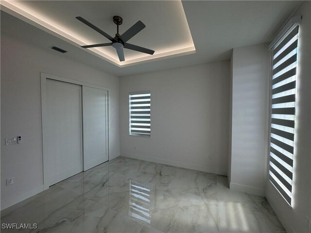 unfurnished bedroom featuring a tray ceiling, a closet, and ceiling fan