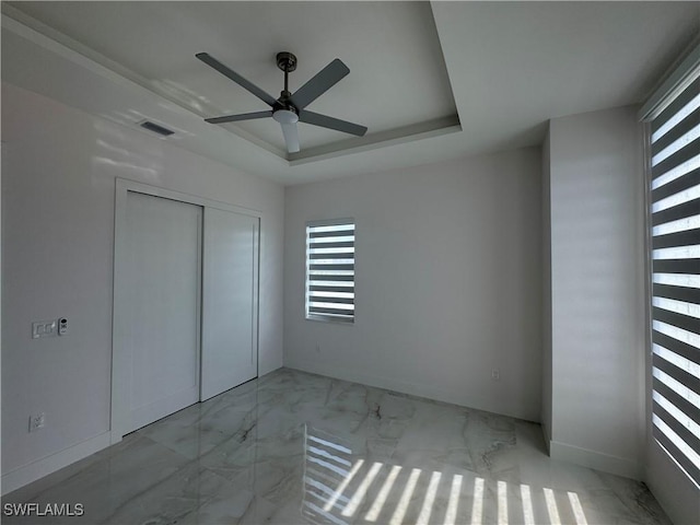 unfurnished bedroom featuring multiple windows, a tray ceiling, a closet, and ceiling fan