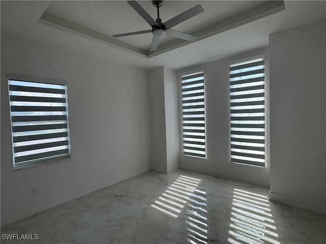 empty room with a raised ceiling, a healthy amount of sunlight, and ceiling fan