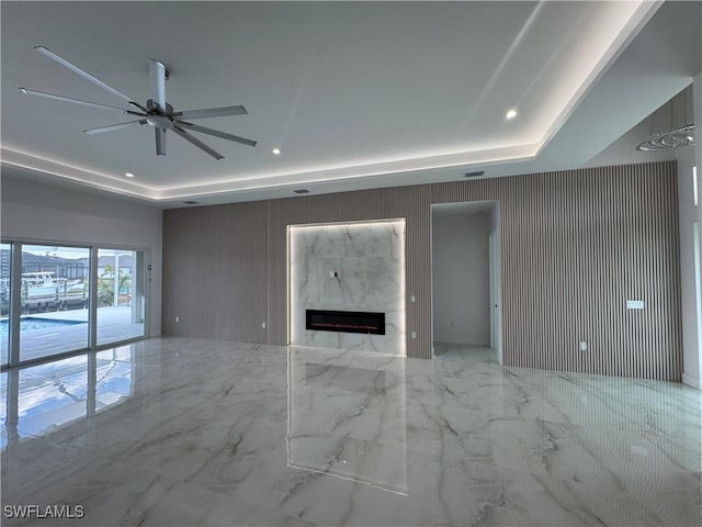 unfurnished living room with a premium fireplace, ceiling fan, and a tray ceiling