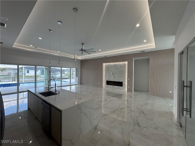 kitchen featuring a kitchen island with sink, a raised ceiling, sink, and hanging light fixtures