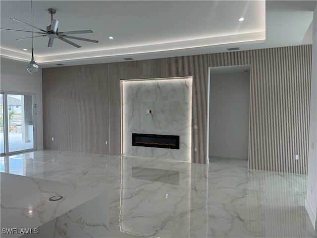 unfurnished living room featuring ceiling fan, a premium fireplace, and a raised ceiling