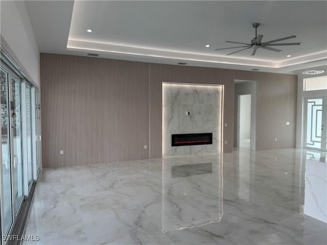 unfurnished living room featuring a raised ceiling, a premium fireplace, and ceiling fan