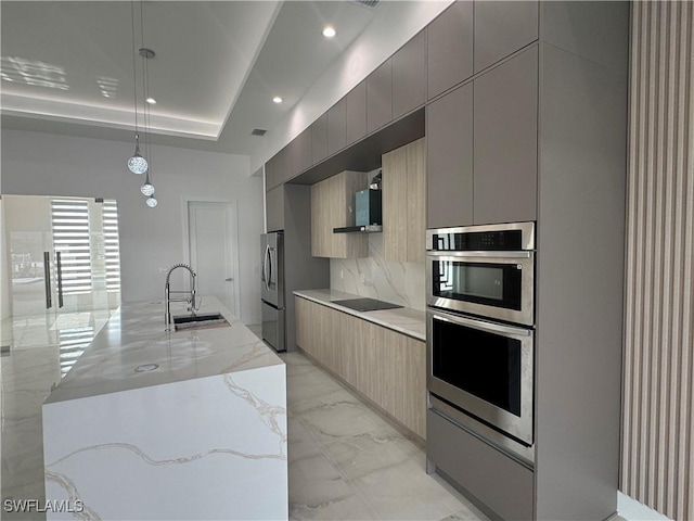 kitchen featuring appliances with stainless steel finishes, pendant lighting, sink, a tray ceiling, and a center island with sink