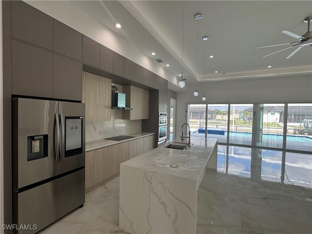 kitchen featuring decorative light fixtures, an island with sink, sink, light stone counters, and stainless steel appliances