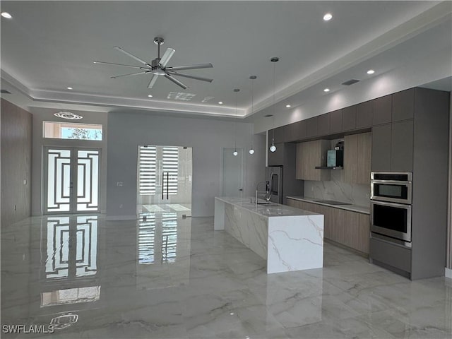 kitchen with a large island, light stone counters, decorative light fixtures, and a raised ceiling