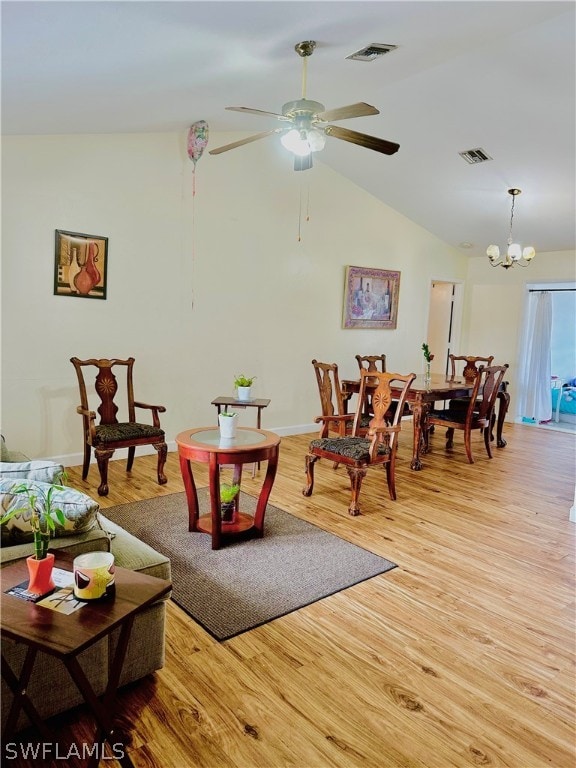 living room with ceiling fan with notable chandelier, vaulted ceiling, and light wood-type flooring