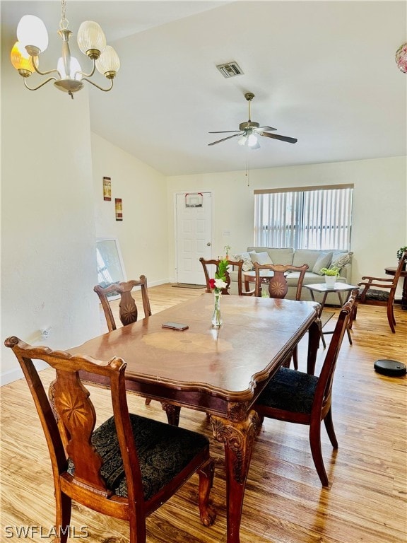 dining area with lofted ceiling, ceiling fan with notable chandelier, and light hardwood / wood-style flooring