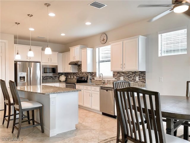 kitchen with appliances with stainless steel finishes, decorative light fixtures, white cabinetry, and a wealth of natural light