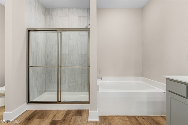 bathroom featuring toilet, wood finished floors, a garden tub, vanity, and a shower stall