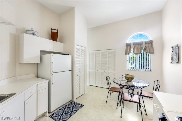 kitchen with white refrigerator, white cabinets, sink, and light tile floors