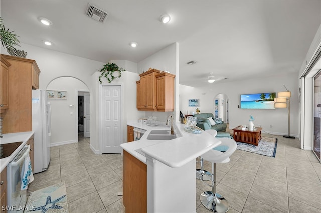 kitchen with white fridge, kitchen peninsula, a breakfast bar area, sink, and light tile floors