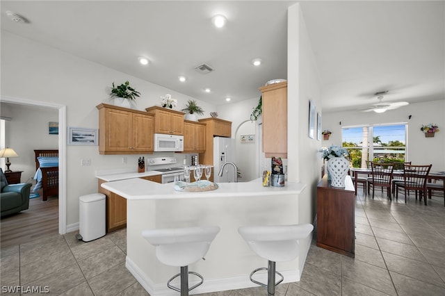 kitchen with ceiling fan, kitchen peninsula, white appliances, light tile floors, and a breakfast bar