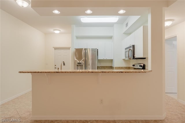 kitchen with kitchen peninsula, stainless steel appliances, a kitchen bar, light stone countertops, and white cabinets