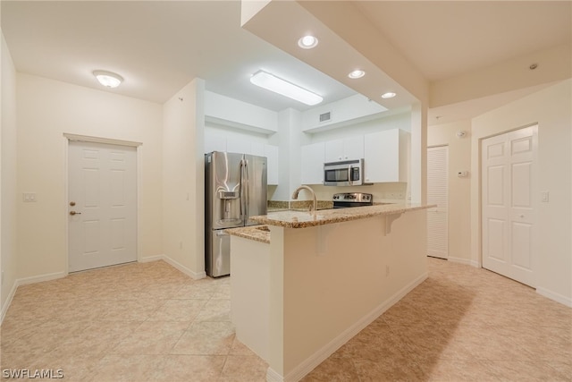 kitchen featuring stainless steel appliances, light stone counters, light tile floors, a kitchen bar, and white cabinetry