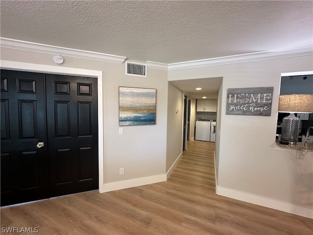 foyer entrance with hardwood / wood-style floors, a textured ceiling, crown molding, and independent washer and dryer