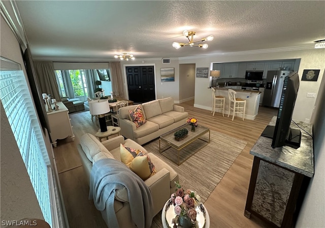 living room featuring light wood-type flooring, a textured ceiling, crown molding, and an inviting chandelier