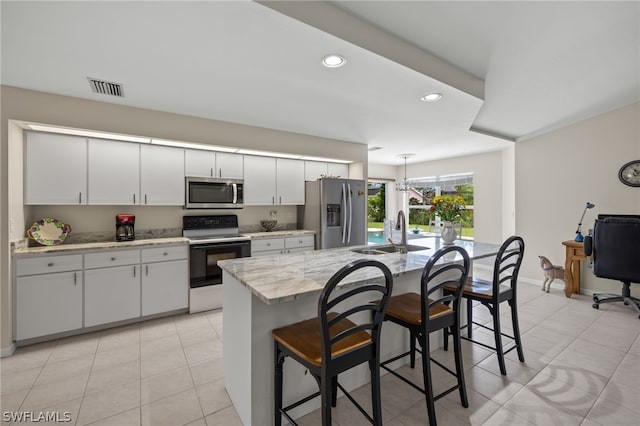 kitchen featuring appliances with stainless steel finishes, a kitchen island with sink, a kitchen bar, sink, and light tile floors