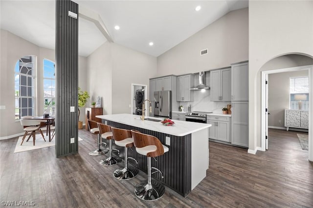 kitchen featuring gray cabinets, a kitchen island with sink, wall chimney range hood, and appliances with stainless steel finishes