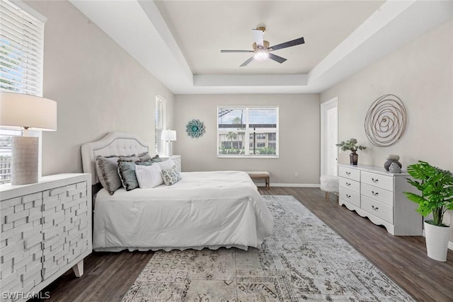 bedroom with dark hardwood / wood-style floors, ceiling fan, and a tray ceiling