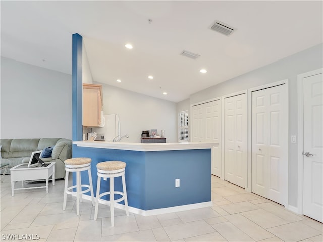 kitchen featuring a kitchen breakfast bar, vaulted ceiling, light brown cabinetry, light tile patterned flooring, and kitchen peninsula