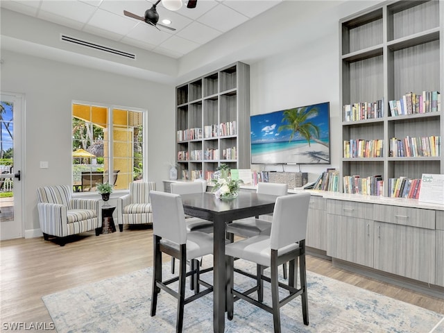 dining space with built in shelves, a paneled ceiling, light hardwood / wood-style floors, and ceiling fan