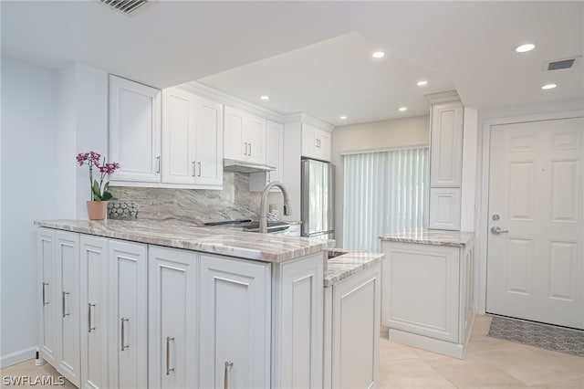 kitchen featuring backsplash, white cabinetry, kitchen peninsula, and stainless steel refrigerator