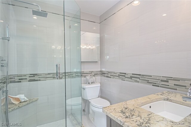 bathroom with vanity, toilet, a shower with door, and tile walls