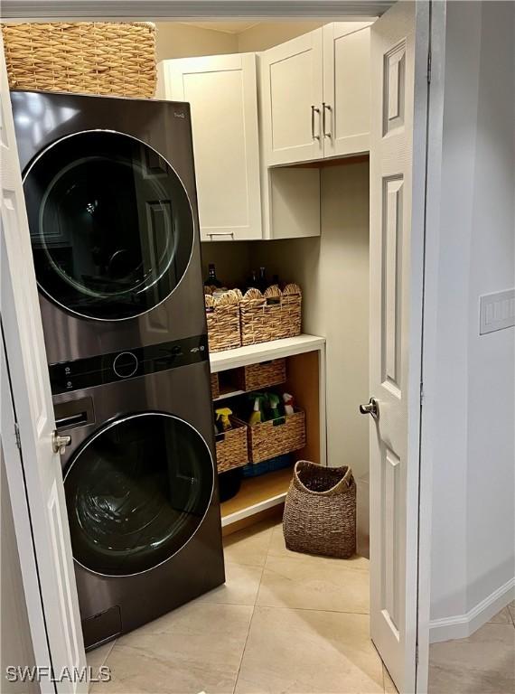 laundry area featuring cabinets, light tile patterned floors, and stacked washer / dryer