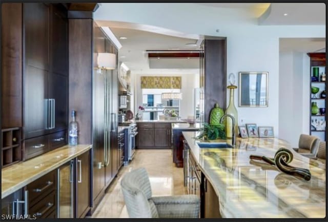 kitchen with dark brown cabinetry, light stone countertops, sink, and stove