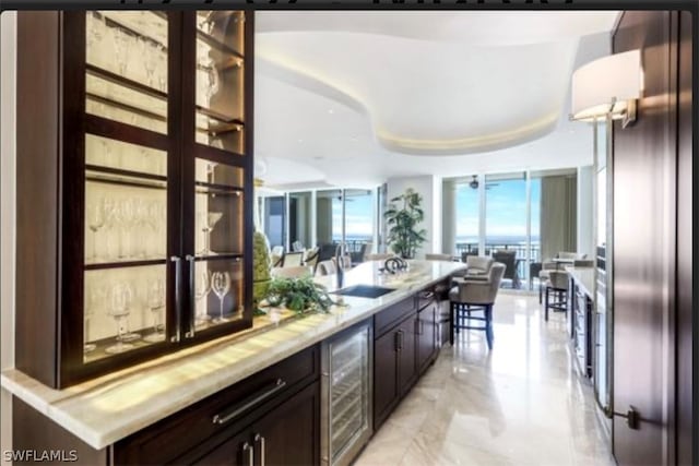 kitchen with a tray ceiling, dark brown cabinets, wine cooler, sink, and light tile floors