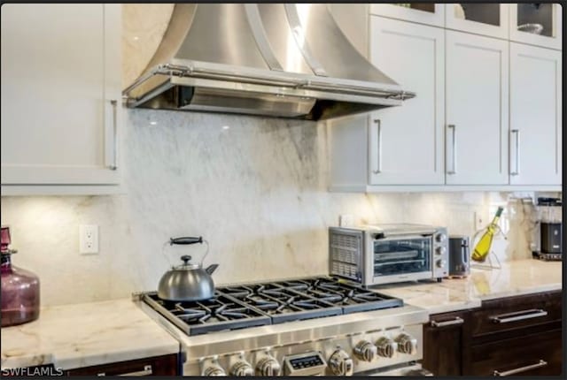 kitchen with dark brown cabinets, range, backsplash, wall chimney range hood, and white cabinets