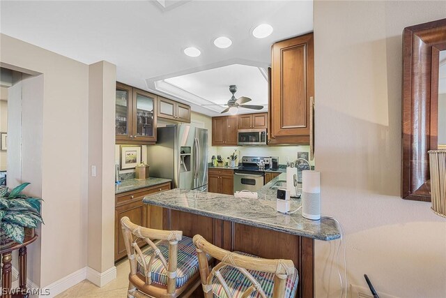 kitchen with ceiling fan, kitchen peninsula, stainless steel appliances, sink, and stone countertops