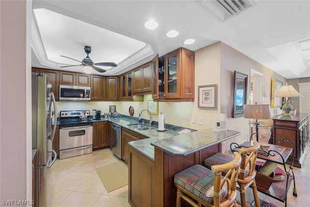 kitchen featuring dark stone countertops, stainless steel appliances, kitchen peninsula, light tile flooring, and ceiling fan