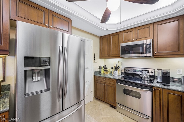 kitchen with dark stone counters, stainless steel appliances, ceiling fan, a raised ceiling, and light tile floors