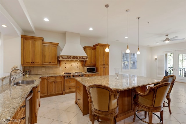 kitchen featuring premium range hood, stainless steel appliances, ceiling fan, sink, and decorative light fixtures