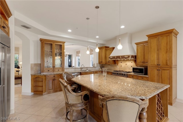 kitchen featuring a kitchen bar, premium range hood, stainless steel appliances, decorative light fixtures, and a center island