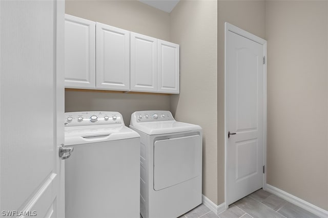 clothes washing area with washing machine and dryer, cabinet space, and baseboards