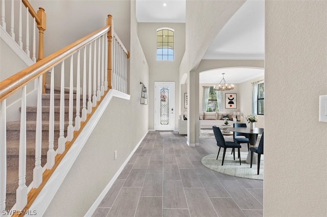 foyer entrance featuring arched walkways, crown molding, stairway, a high ceiling, and baseboards