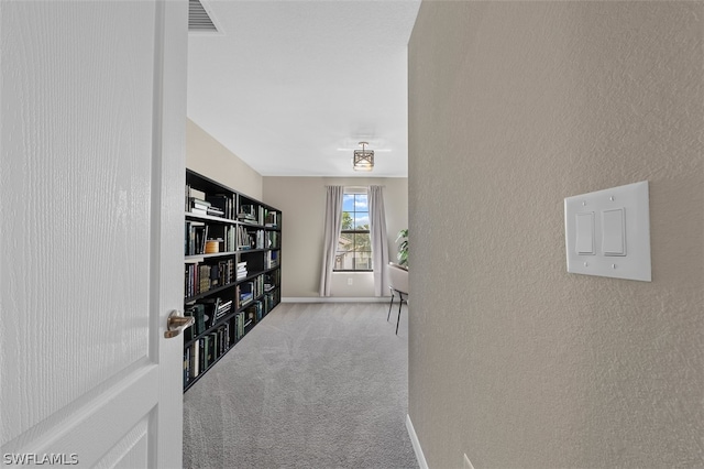 hallway featuring a textured wall, carpet, visible vents, and baseboards