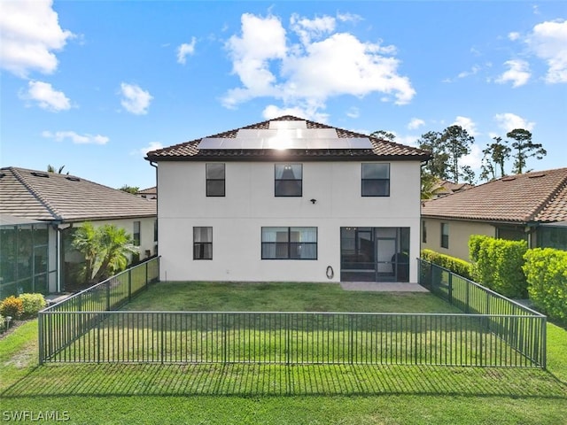 back of house with a fenced backyard, roof mounted solar panels, a lawn, and stucco siding