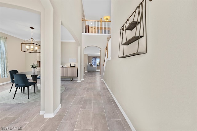 corridor with arched walkways, an inviting chandelier, ornamental molding, wood tiled floor, and baseboards