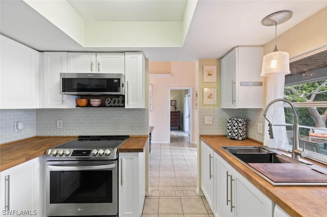 kitchen with decorative light fixtures, light tile patterned floors, appliances with stainless steel finishes, sink, and butcher block counters